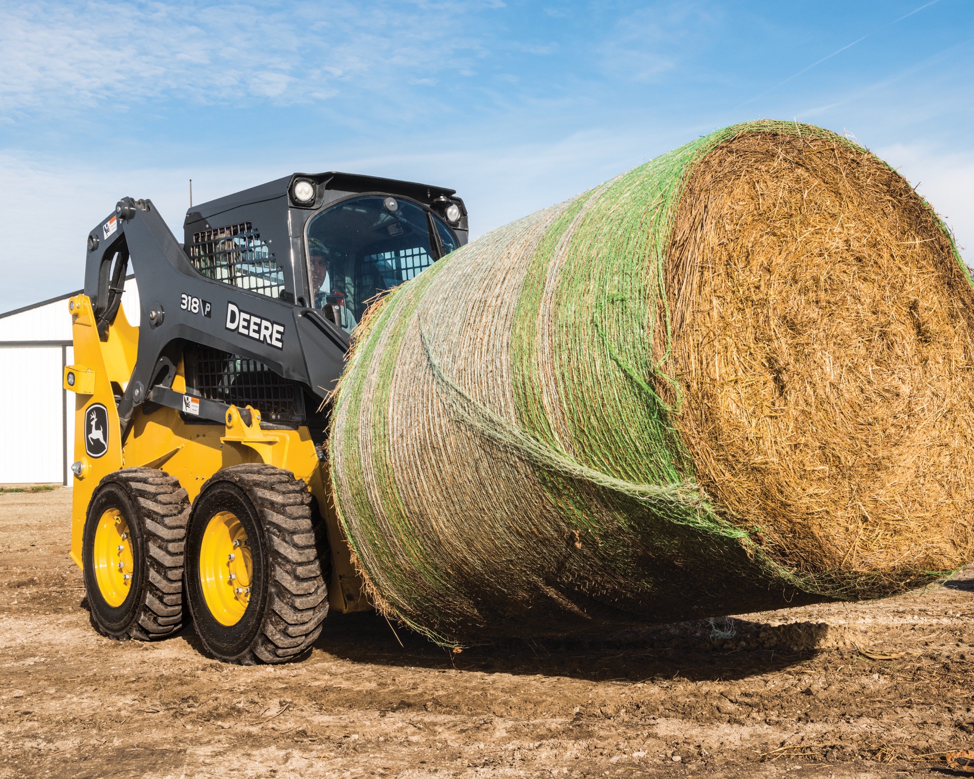 John Deere 318 P skid steer carrying a round hay bale